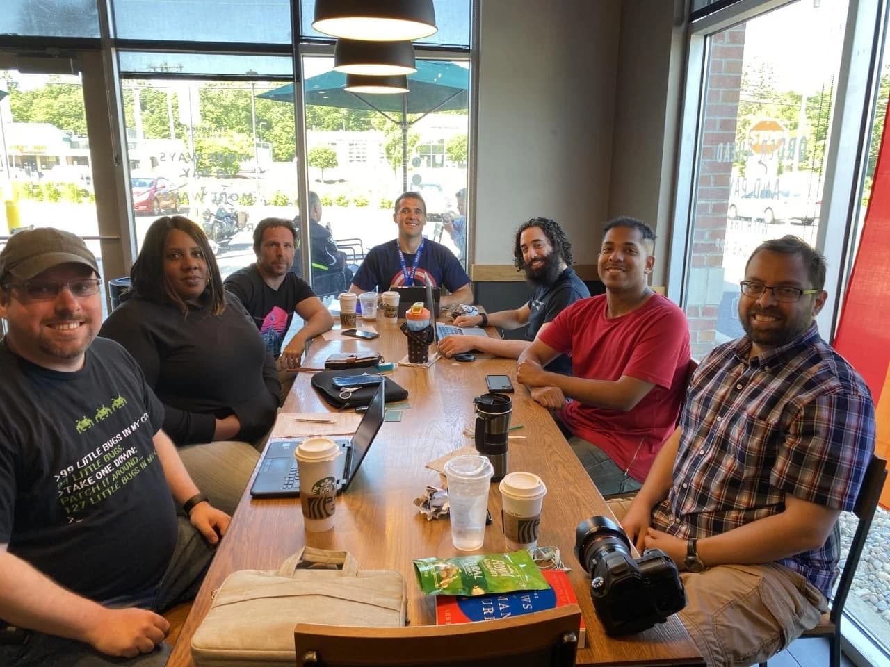 Software community members seated on both sides of a café table with laptops.