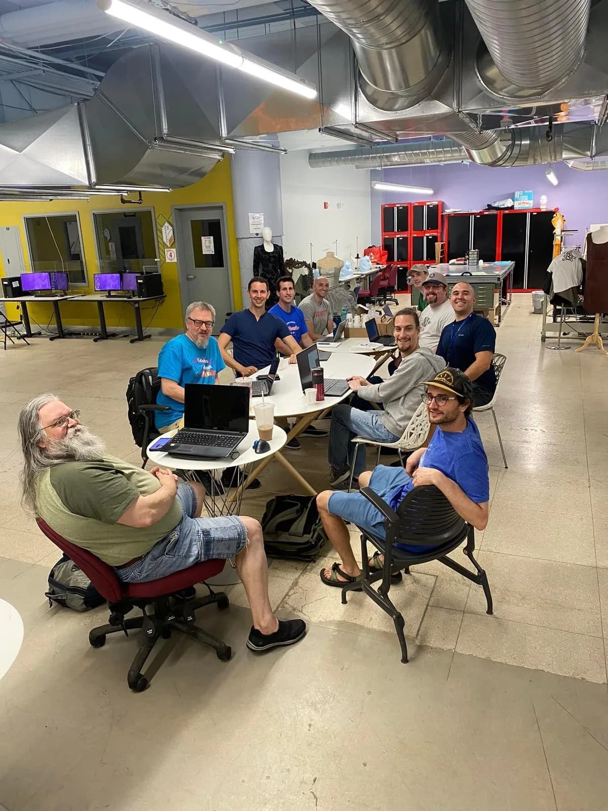 Software community members gathered around laptops in a shared workshop space.