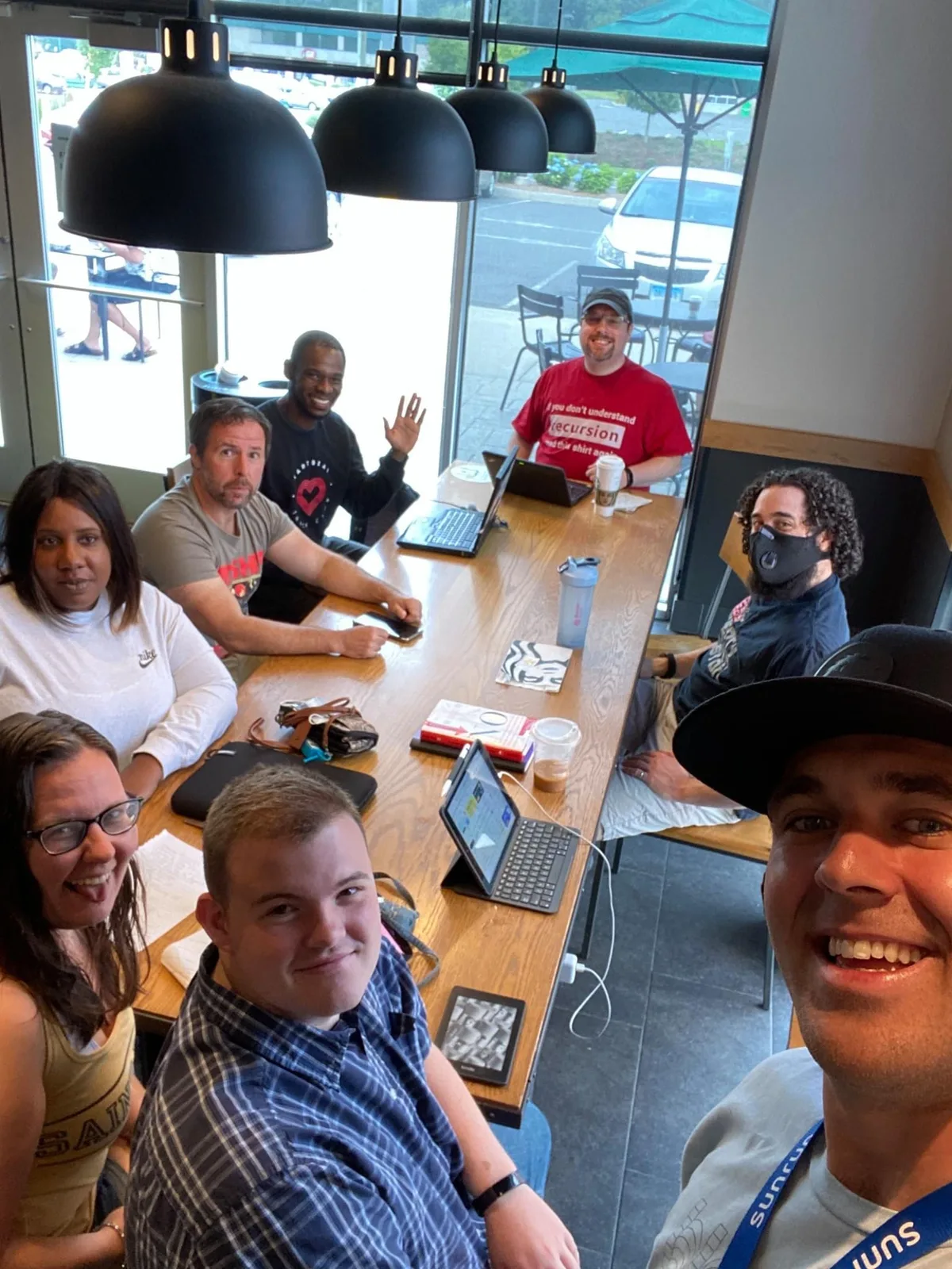 Software community members taking a group selfie around a café table with laptops.